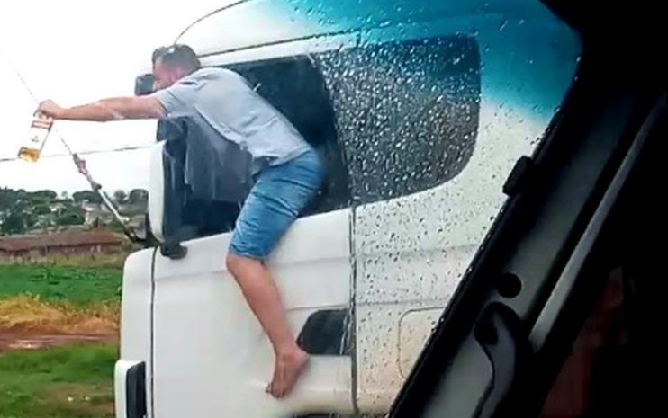 Caminhoneiro é filmado com corpo para fora de veículo com garrafa de bebida na mão enquanto dirige 4